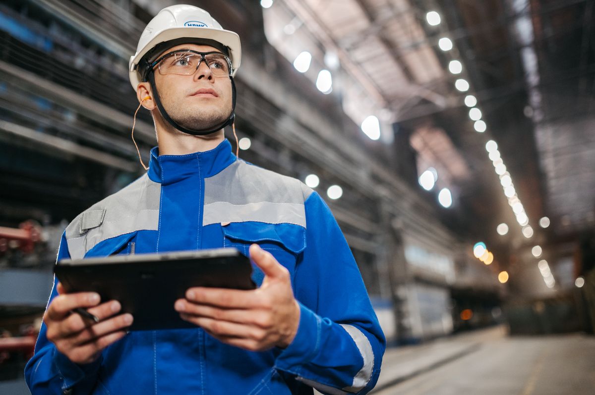 Operator in safety gear reviewing data on a tablet in an industrial facility